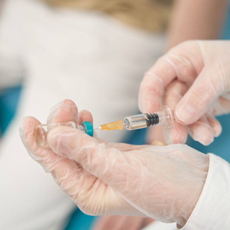 Cropped head close up of female hands in rubber gloves holding syringe with medicine for man
